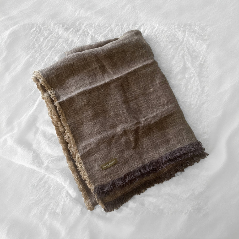 Linen herringbone throw in earthy brown with fringed edges, folded on a light textured surface.