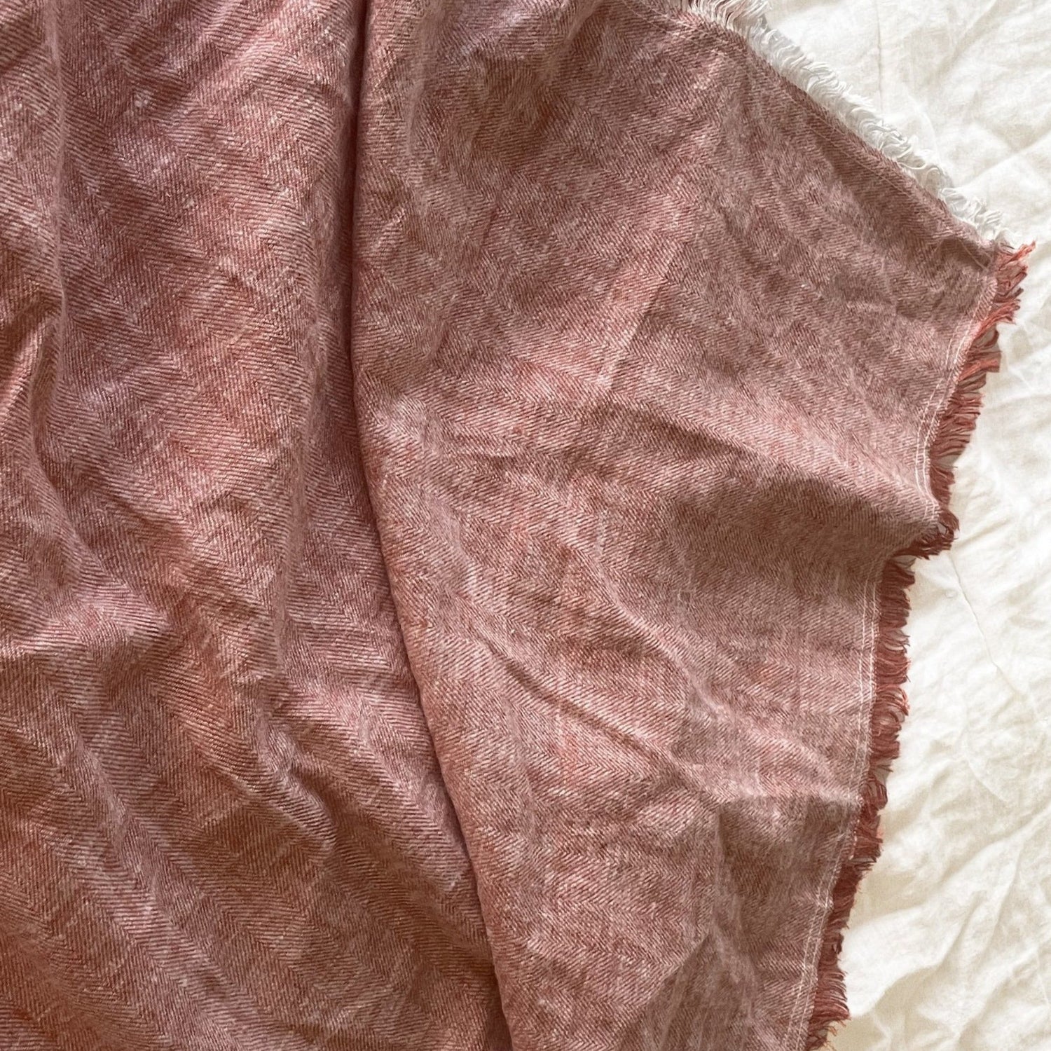 Terracota linen herringbone throw with frayed edges, draped on a light textured surface.