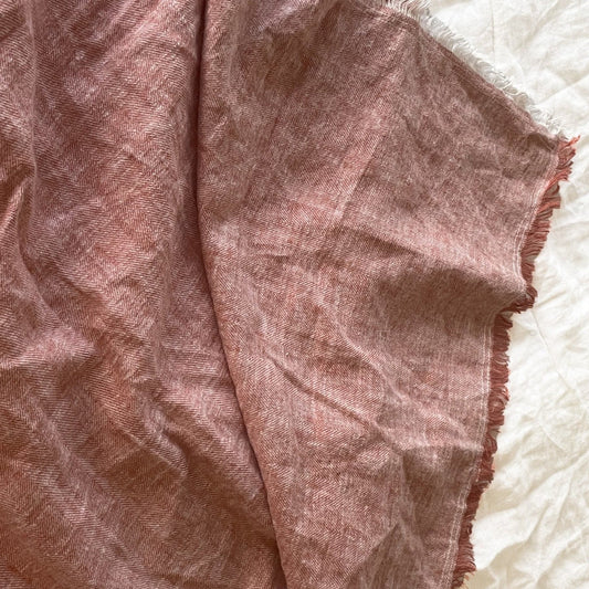 Terracota linen herringbone throw with frayed edges, draped on a light textured surface.