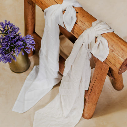 Two linen swaddles, one white and one blue, are draped over a wooden bench with a vase of purple flowers beside them.